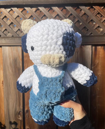 crocheted plushie of a white cow with dark blue spots and denim blue overalls