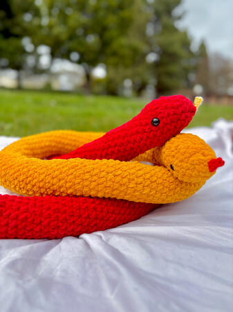 large crocheted snakes in bright red and golden yellow, coiled around each other on a white blanket
