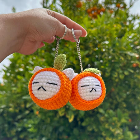 crocheted keychain of a white cat head in a tangerine-themed hood