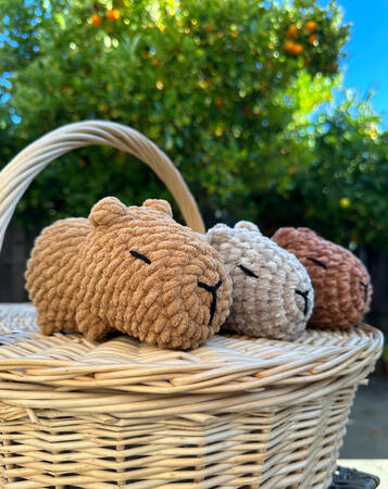 three capybaras in varying shades of brown sitting on top of a picnic basket